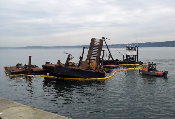 A fuel containment boom surrounds a barge that partially sank in South Whidbey Harbor Wednesday. A large crane onboard fell into the water.