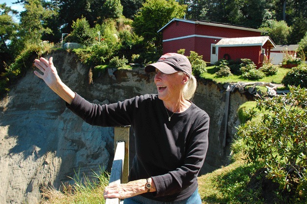 Langley resident Rosalie Ballinger waves hello to one of the many boats passing by her South Whidbey home. The huge portion of the high-bank property has been consumed by erosion from an underground spring.