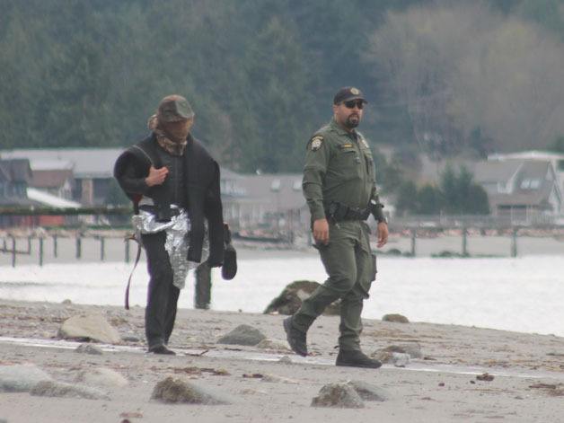 An Island County Sheriff’s Office deputy walks with an unidentified man on the beach at Mutiny Shores in Freeland Friday afternoon.