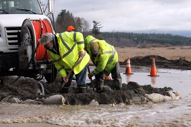 Island County Public Works employees Scott Endres and Kyle Peters create a dike to divert overflowing water on Double Bluff Road. Heavy rain on Thursday caused a catch basin to overflow across the road. One lane of traffic was blocked during the work.