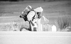 A Navy hazardous materials specialist reaches for an open bottle of acid dumped on Highway 525 Wednesday morning.