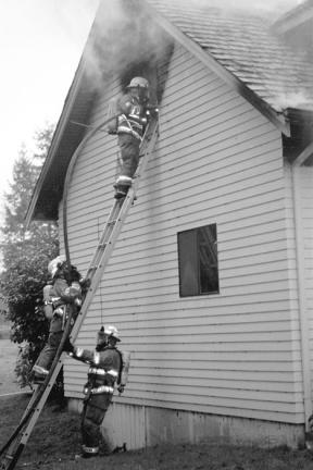 Fire District 5 firefighters climb the side of a two-story home on Classic Road in Greenbank Wednesday morning to try to douse a fire. The David and Julie Jansen residence was unoccupied at the time and was a total loss.