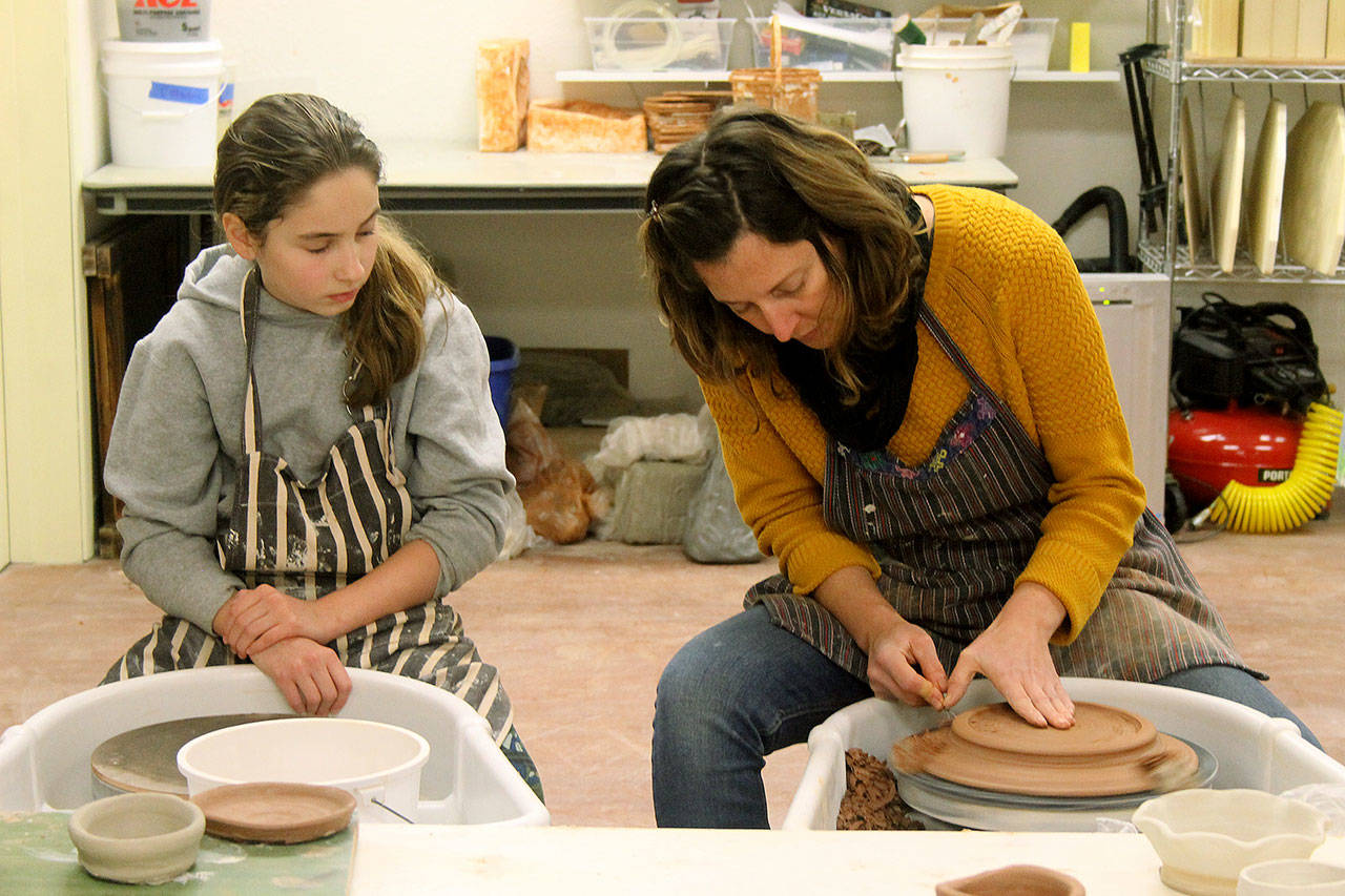 Photo by Kira Erickson/South Whidbey Record                                Molly Stahl, left, watches as Cara Jung shows kids how to trim their pottery creations.