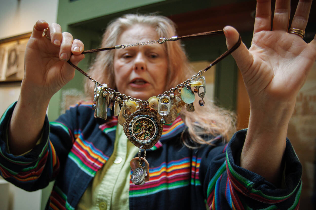 Photo by David Welton
Mixed media artist Sarah Dial Primrose shows off a necklace made of rocks, shells, pop tabs and a crushed Starbucks cap that she has dubbed “Beach Party.” Her art is on display as part of the “Rags, Rubbish, and Refuse” exhibit at the Bayview Cash Store.