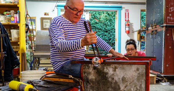 Photo by David Welton
John de Wit shapes a piece of glass while Catherine Marshall blows the glass.