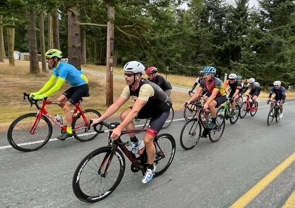 A group of Tour de Whidbey bikers ride on a Whidbey road surrounded by a green landscape. (Photo from the Tour de Whidbey website)